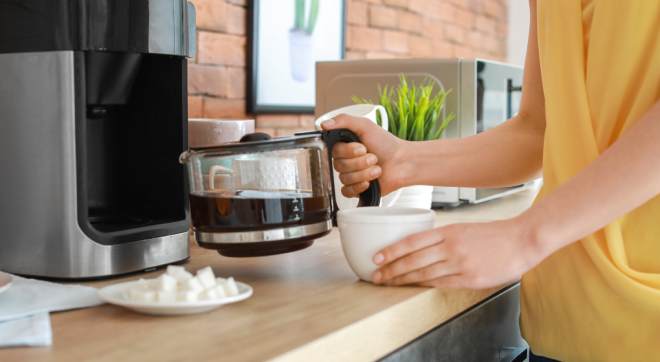 Person schenkt Kaffee aus einer Kaffeemaschine in eine Tasse als Teaserbild zum Thema Kaffeemaschine entkalken und Gerätepflege in der Küche
