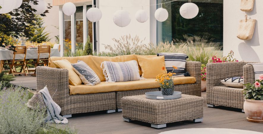 Saubere Gartenmöbel aus Rattan auf einer gepflegten Terrasse mit Sofa, Sessel und Tisch als Teaserbild zum Thema Gartenmöbel reinigen und Terrassenpflege