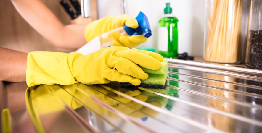 Hände mit gelben Reinigungshandschuhen reinigen eine Edelstahloberfläche mit Schwamm und Reiniger als Teaserbild zum Thema Edelstahl richtig reinigen und pflegen