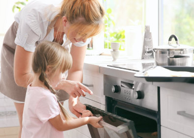 Frau und Kind reinigen gemeinsam einen Backofen in einer hellen Küche als Teaserbild zum Thema Backofen reinigen und Küchenpflege