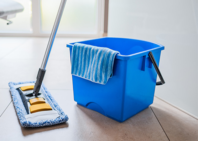 Blauer Putzeimer mit Reinigungstuch und Bodenwischer auf Fliesenboden im Badezimmer als Symbol für einen strukturierten Putzplan im Haushalt